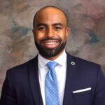 Headshot_Berry_Cornelius - Texas Healthcare Trustees Smiling man in a navy suit light blue patterned tie white shirt and lapel pin in a portrait photo