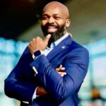 Headshot_Greenhill_Richard - Texas Healthcare Trustees Smiling bald man with a beard in a navy suit arms crossed wearing a smartwatch