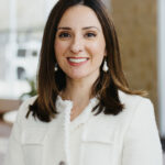 THA2025_SaraGonzalez - Texas Healthcare Trustees Woman with long brown hair smiling in a white textured jacket indoors