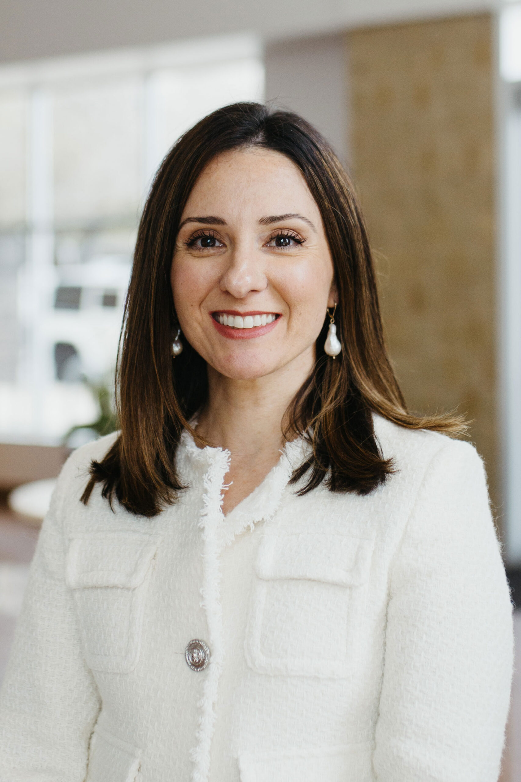 Woman with long brown hair smiling in a white textured jacket indoors