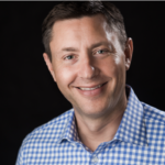 david hilderbrand - Texas Healthcare Trustees Smiling man in a blue checkered shirt against a dark background head and shoulders portrait